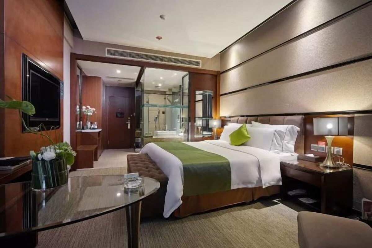 A hotel room with a bed, bedside table, lamp, and a television.
