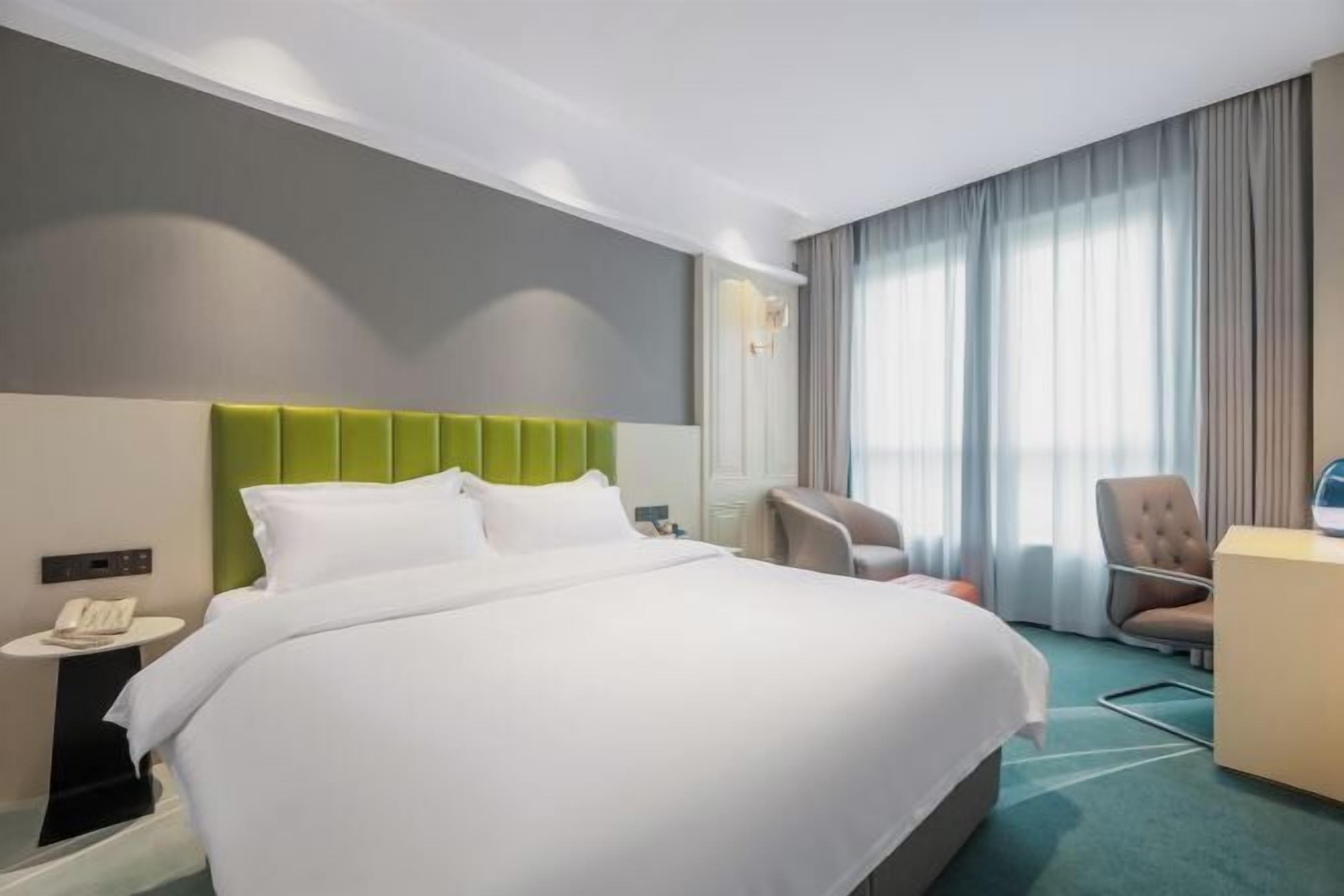 A hotel room with a bed, a desk, a chair, a phone, and a window with curtains.