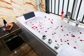 A modern bathroom with a large bathtub, rose petals, a bottle of champagne, and a rose vase. - Liwan International Hotel (Chengdu)