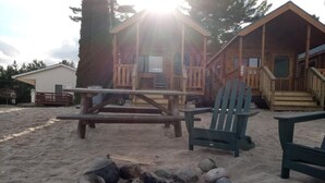 Una cabaña de madera con un porche, una mesa de picnic y un brasero.
