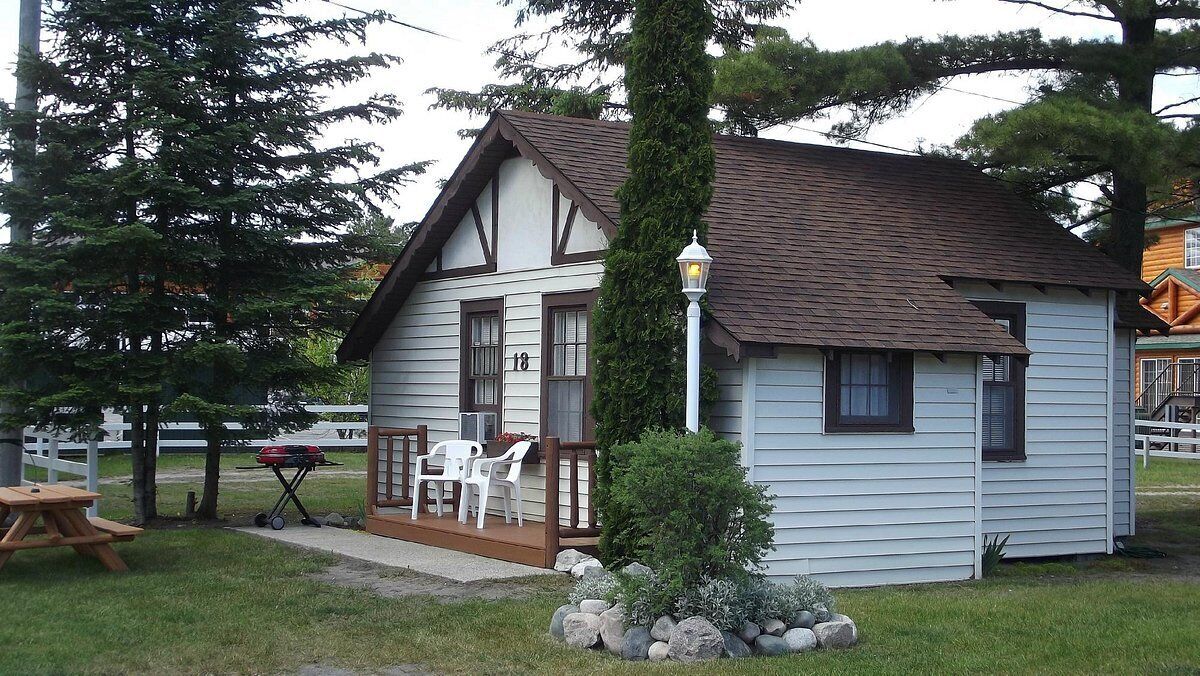 A small, single-story house with a porch, numbered 18, surrounded by trees and a picnic table.
