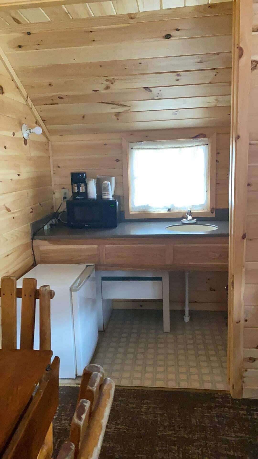 Une petite cabane en bois comprenant un coin cuisine, une fenêtre et un petit réfrigérateur.