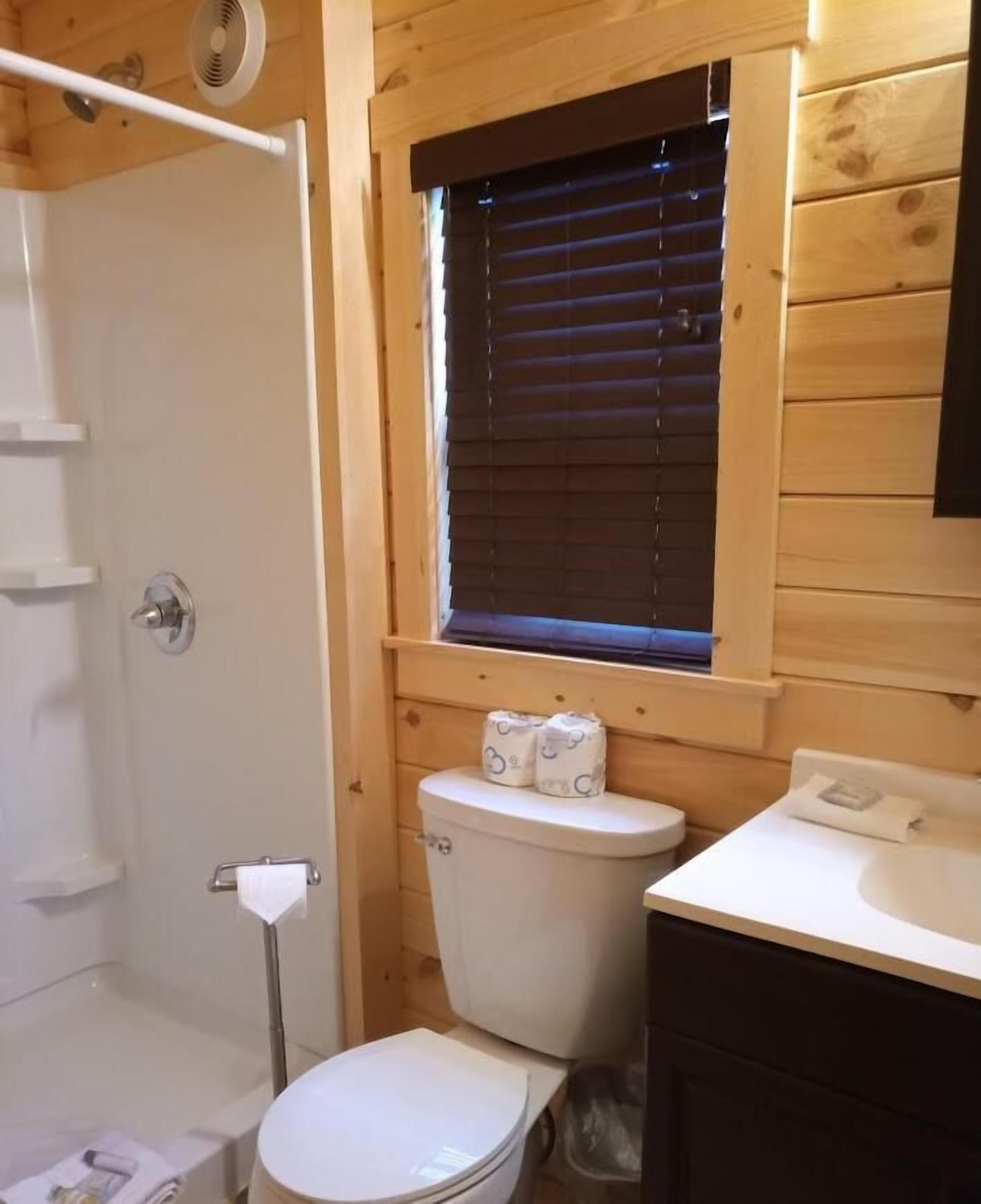 A small, compact bathroom with a white toilet, a sink, and a window with blinds.