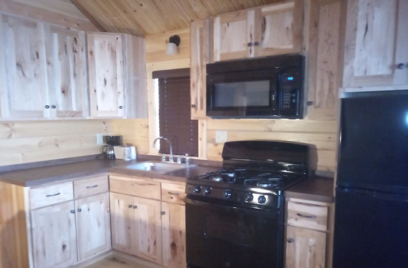A kitchen with wooden cabinets, a black stove, a microwave, and a refrigerator.