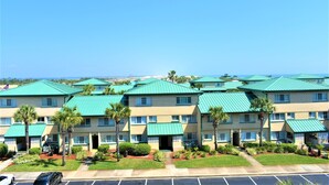 A multi-story hotel with a green roof and palm trees in the courtyard. - Destin West Vacations (Fort Walton Beach)