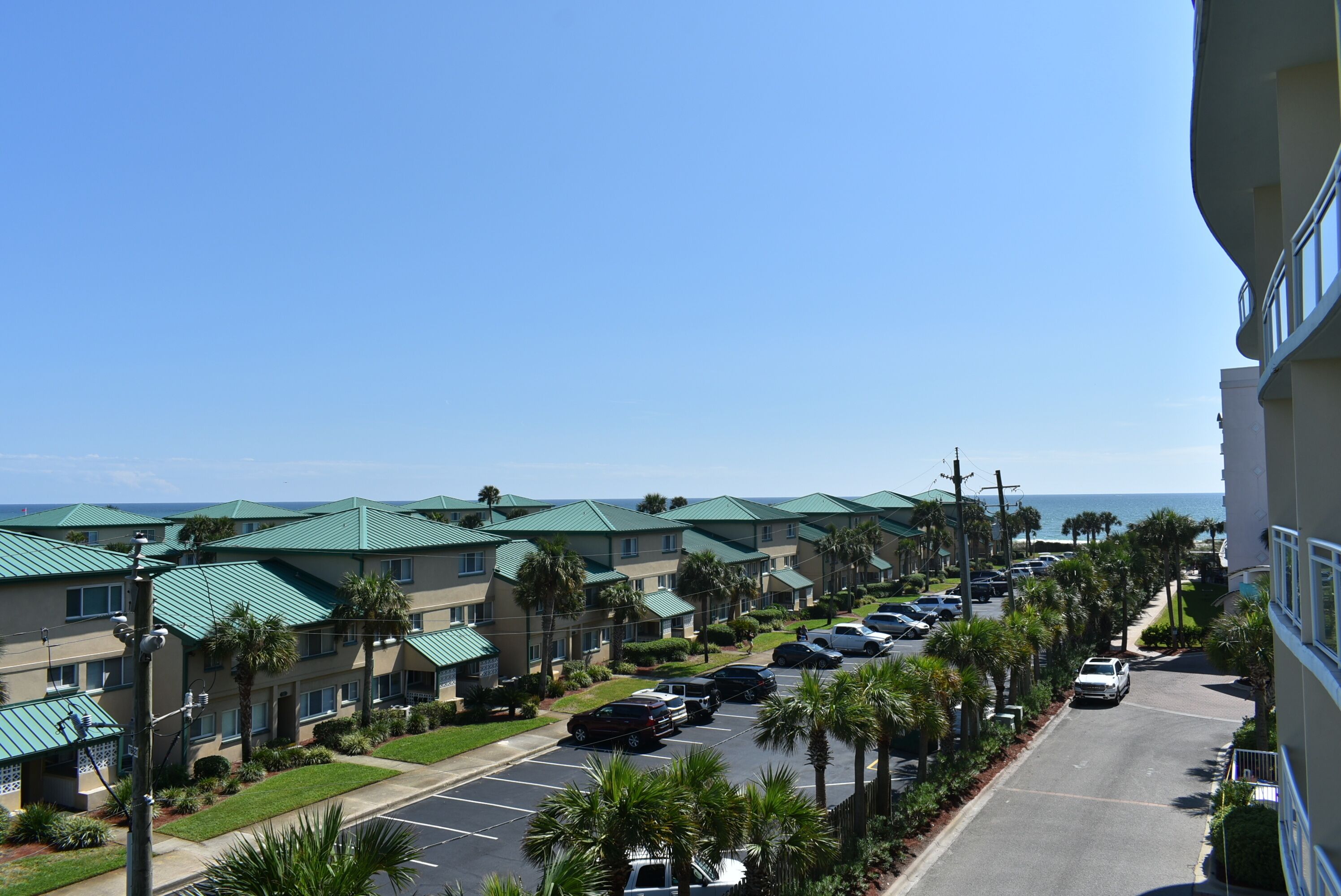 A row of hotel buildings with green roofs, a parking lot, and a view of the ocean.