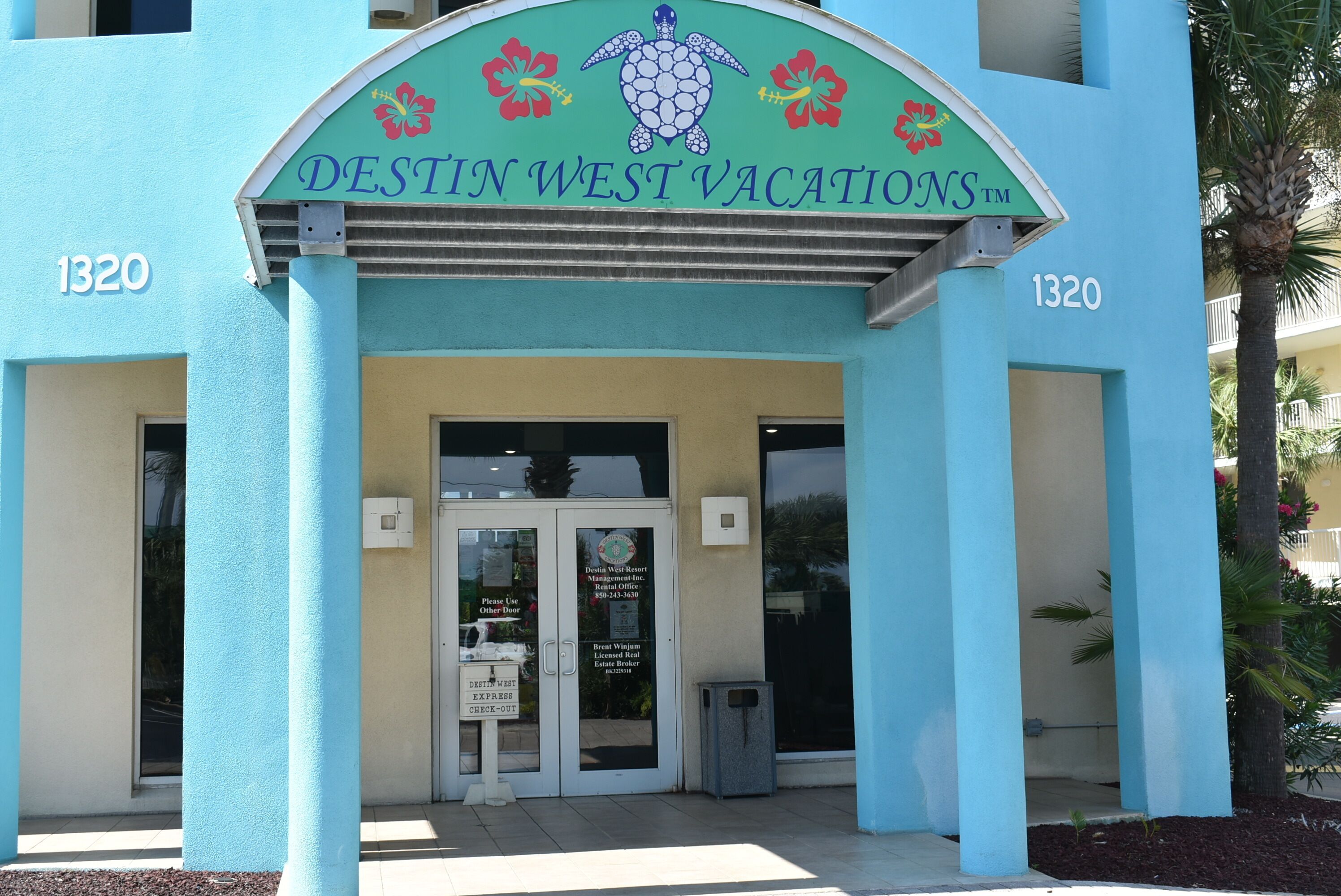 Exterior de Destiny West Vacations, con fachada color turquesa, un logo de tortuga y el número 1320.