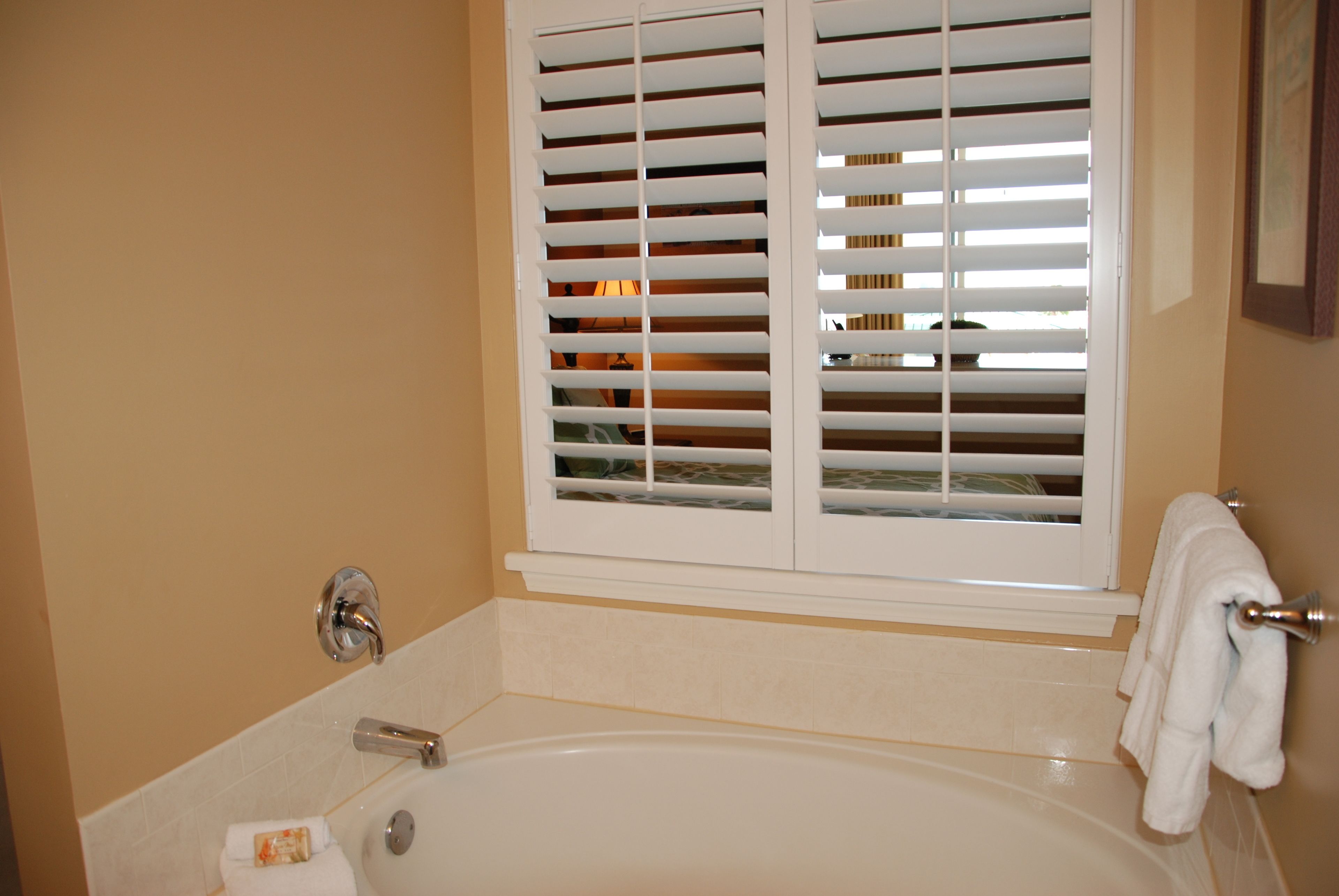 Un baño con una bañera, una ventana con persianas y un perchero para toallas.