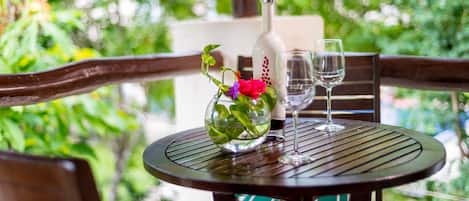 A round table with a bottle and two glasses, surrounded by wooden chairs with green cushions.