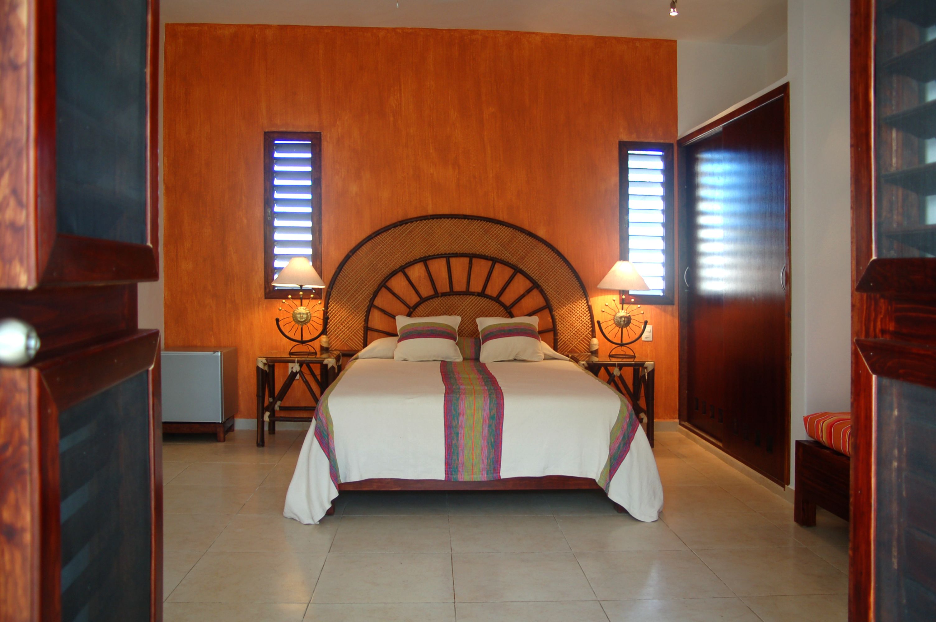 Una cama grande con cabecera de madera, dos mesitas de noche con lámparas y vistas a una pared y puerta de madera.