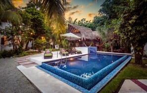 A swimming pool with a thatched-roof structure, surrounded by lush greenery and a well-maintained lawn. - Villas El Encanto Cozumel (Cozumel)