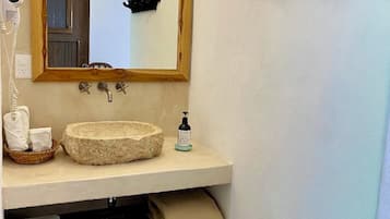 A bathroom with a wooden-framed mirror, a stone sink, a hairdryer, and a towel rack.