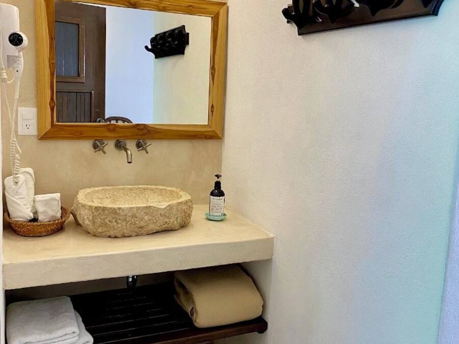 A bathroom with a wooden-framed mirror, a stone sink, a hairdryer, and a towel rack.