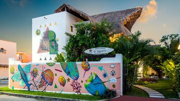 A building with a colorful mural, a thatched roof, and a sign for Hotel-Villas El Encanto.