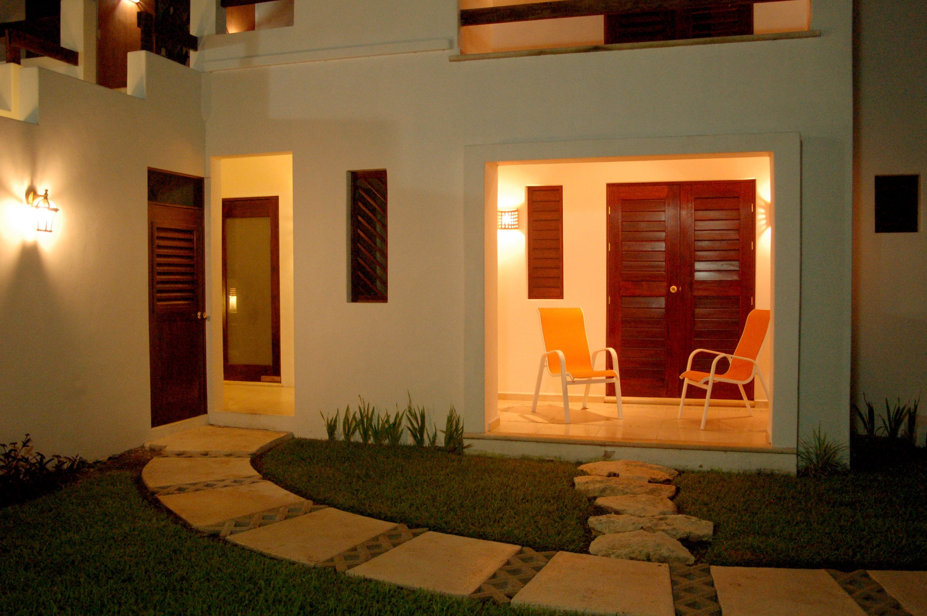 A modern house with a stone pathway leading to a wooden door and a set of double doors with an orange chair outside.