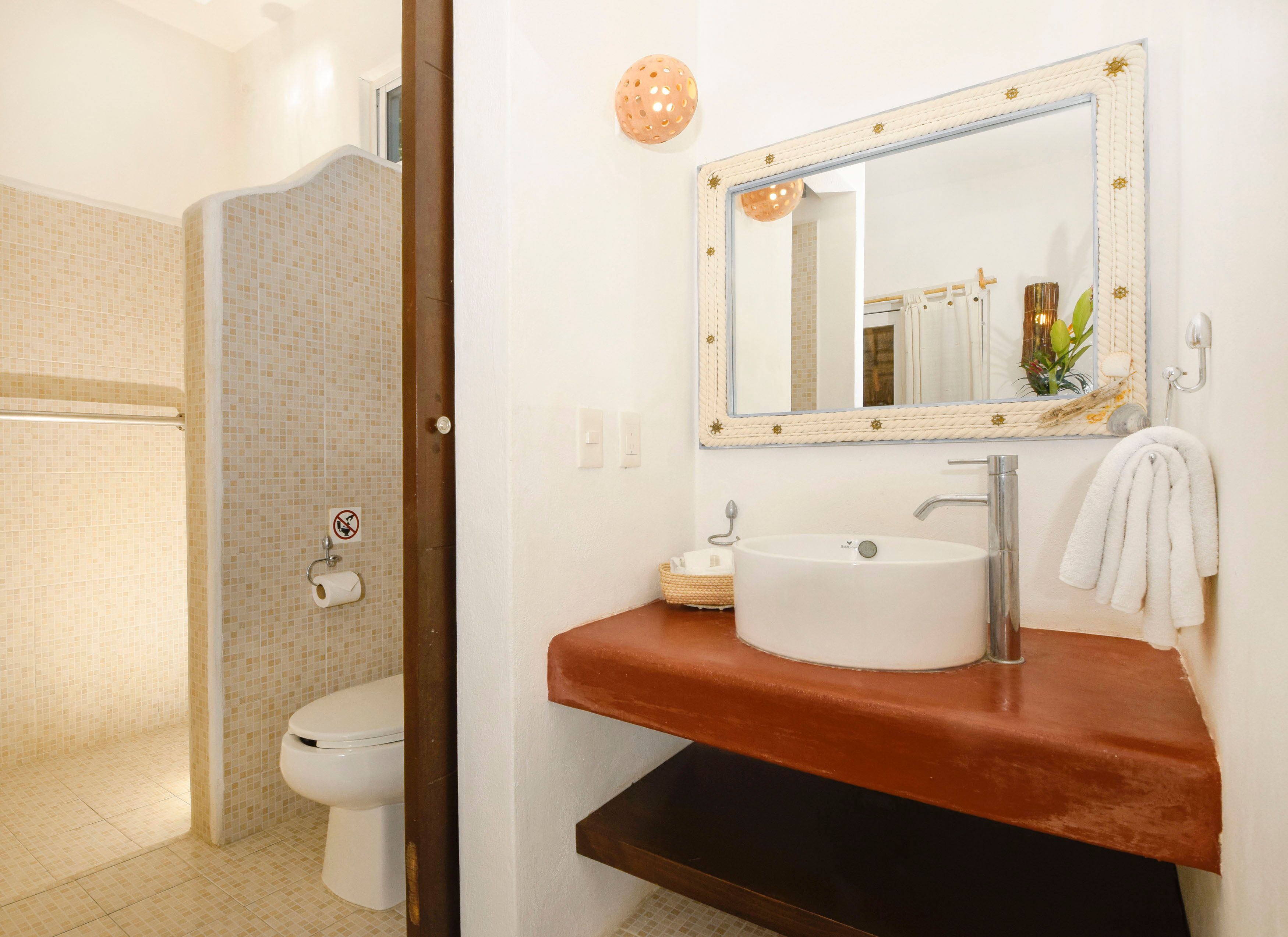 Un baño con un inodoro blanco, un lavamanos con encimera marrón y un espejo con marco decorativo.