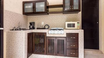 A kitchen with a tiled backsplash, dark wooden cabinets, a gas stove, a microwave, and a coffee maker.
