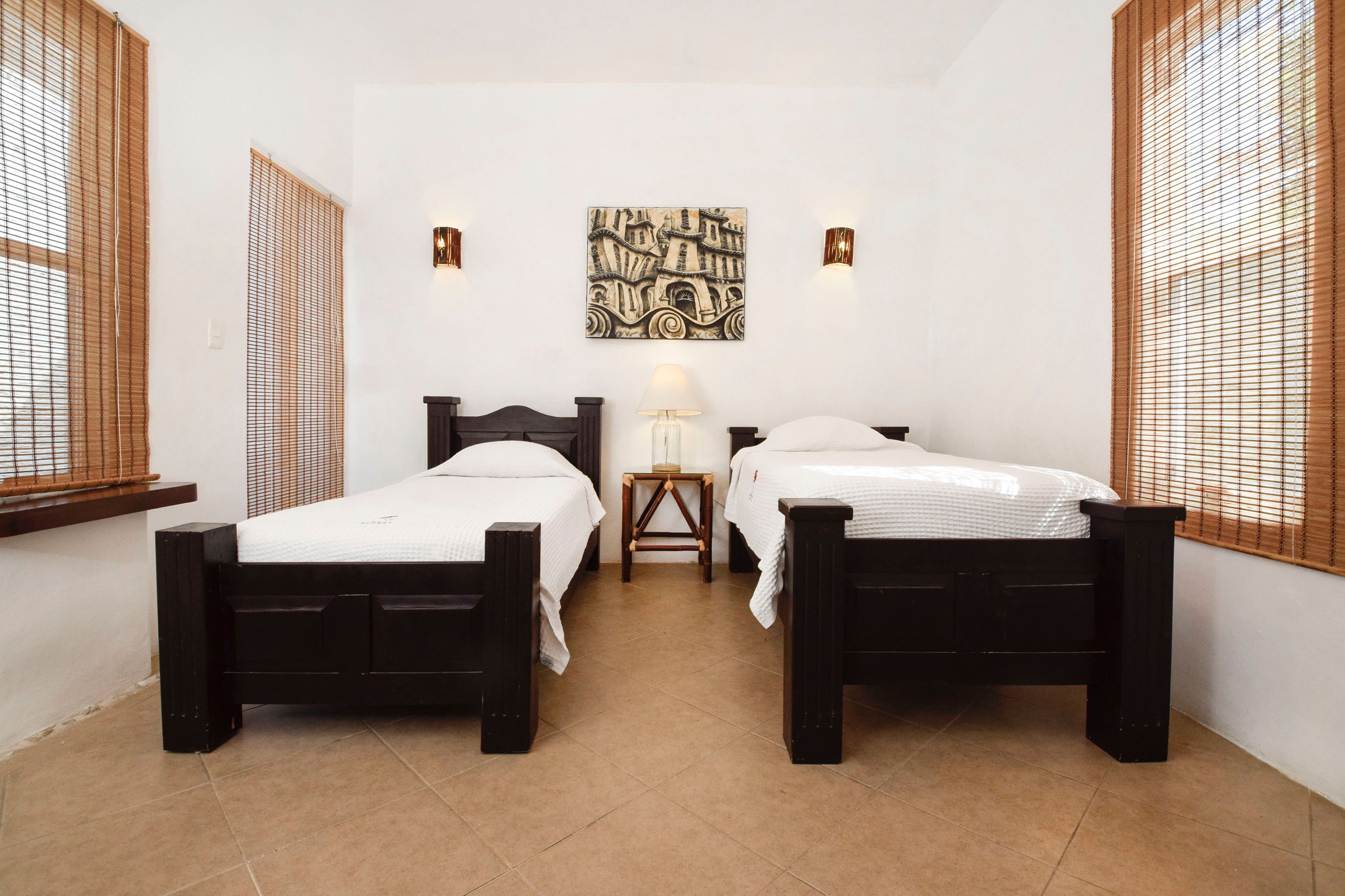 A room with two beds, a nightstand, a lamp, and a wall-mounted artwork.