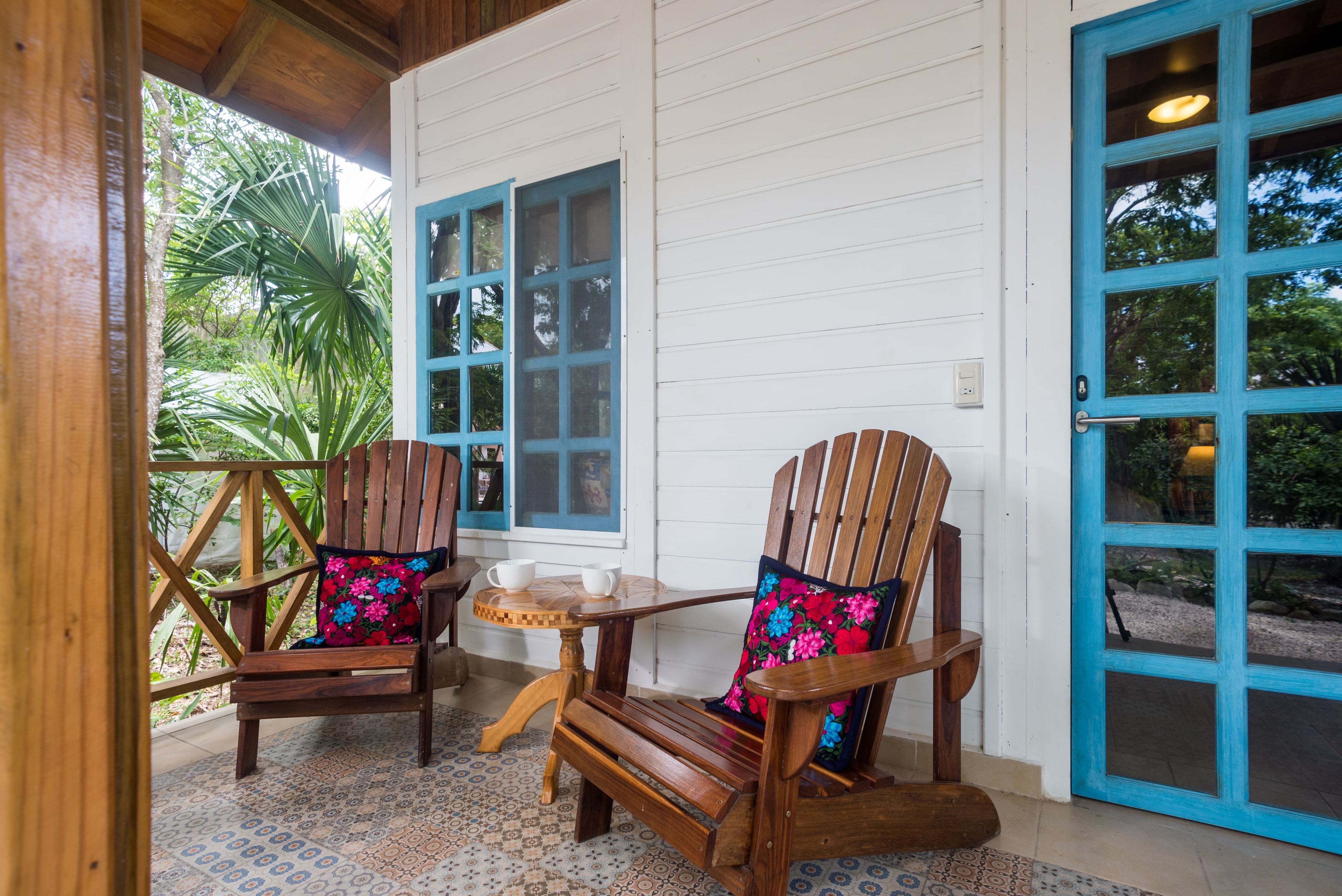 Une véranda en bois avec deux fauteuils Adirondack, une petite table ronde et une porte bleue.