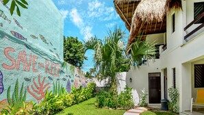 Un patio con un mural, techo de paja y un edificio blanco con puerta y ventanas.