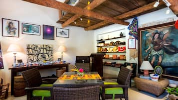Un comedor con mobiliario de mimbre, una mesa con un centro de mesa floral y obras de arte en las paredes.