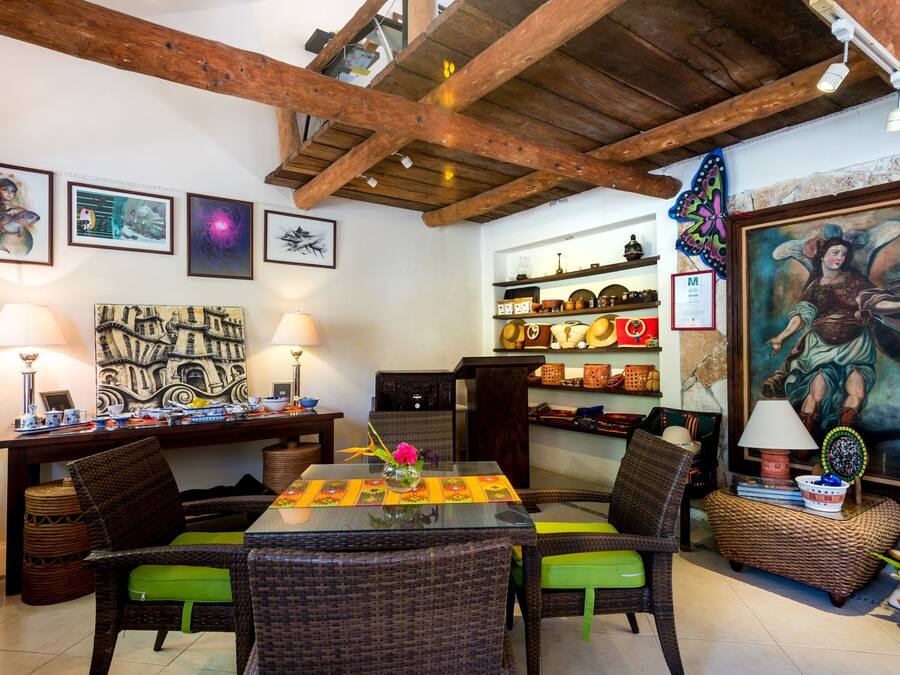 Un comedor con mobiliario de mimbre, una mesa con un centro de mesa floral y obras de arte en las paredes.
