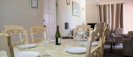 A dining area with a table set for four, chairs, a wine bottle, and a clock on the wall.