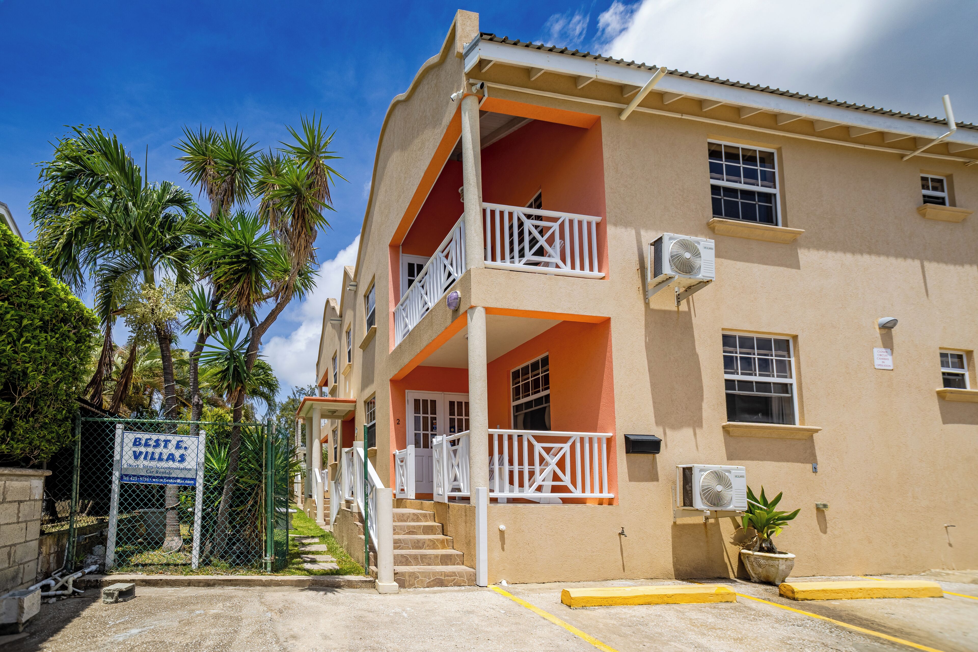 Un immeuble de deux étages doté de balcons, de climatiseurs et d’une enseigne indiquant « Best E. Villas ».