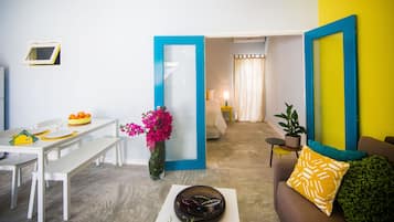 A living room with a dining area, a sofa with a patterned cushion, a potted plant, and a mirror with a blue frame.