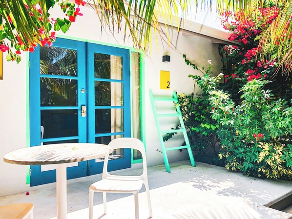 A small outdoor seating area with a table and chairs, a blue door, and a yellow number sign. - Bubali Bliss Studios & Villas (Noord)
