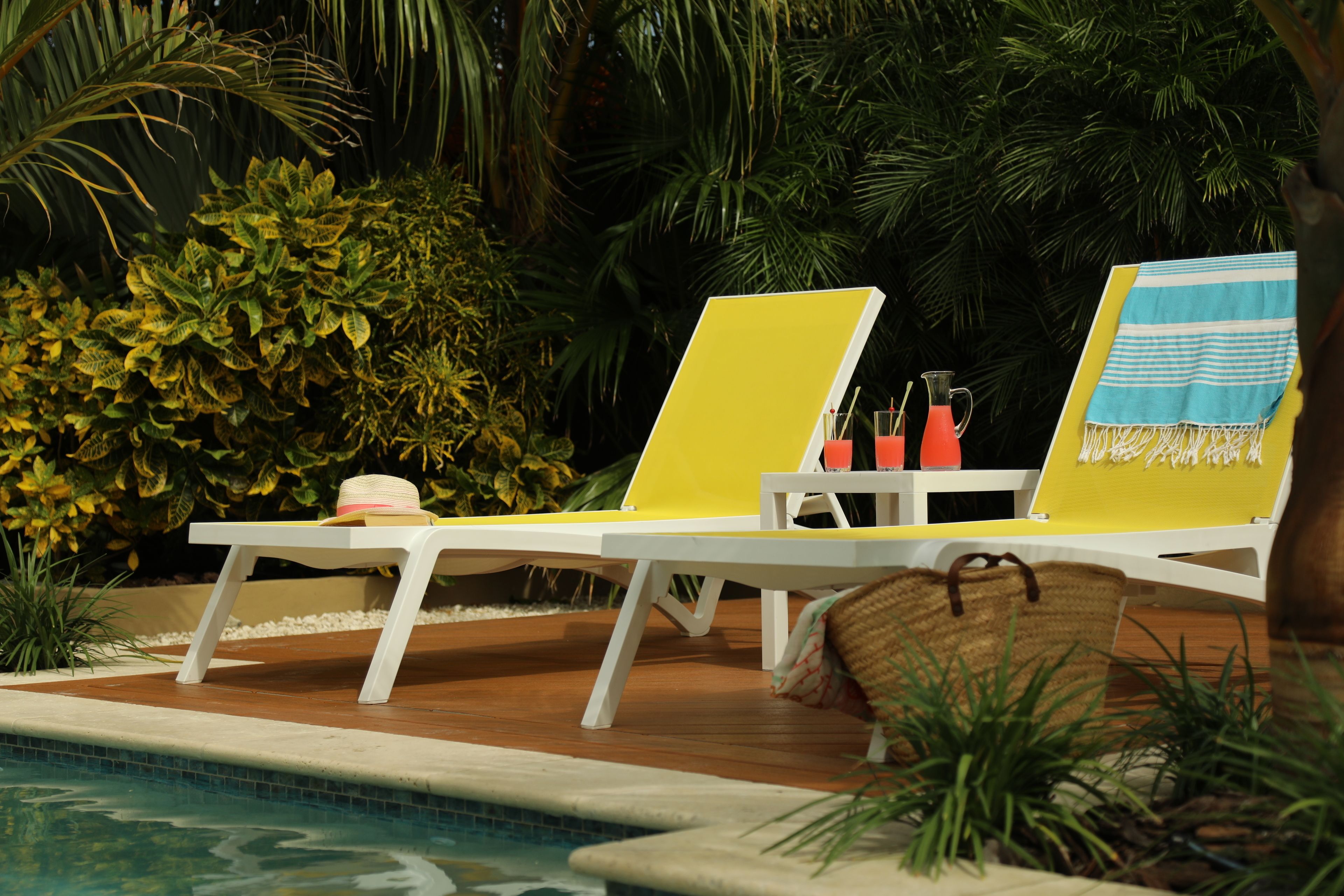 Two yellow lounge chairs by a pool with a straw hat and a woven basket on the right.