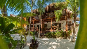 A traditional wooden structure with a thatched roof, surrounded by palm trees and tropical plants.