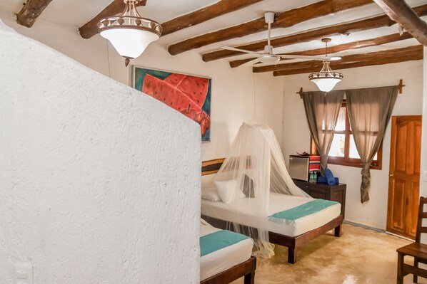 Una habitación con dos camas, vigas de madera, un ventilador de techo y un cuadro en la pared.