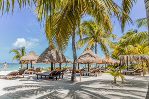 A beach with thatched umbrellas, wooden lounge chairs, and palm trees. - Zomay Beachfront Hotel Holbox (Isla Holbox)