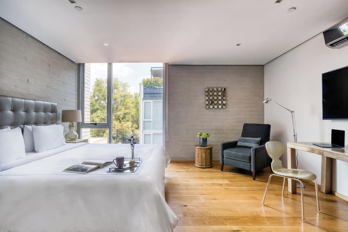 A modern hotel room with a large bed, a desk, a chair, and a TV.