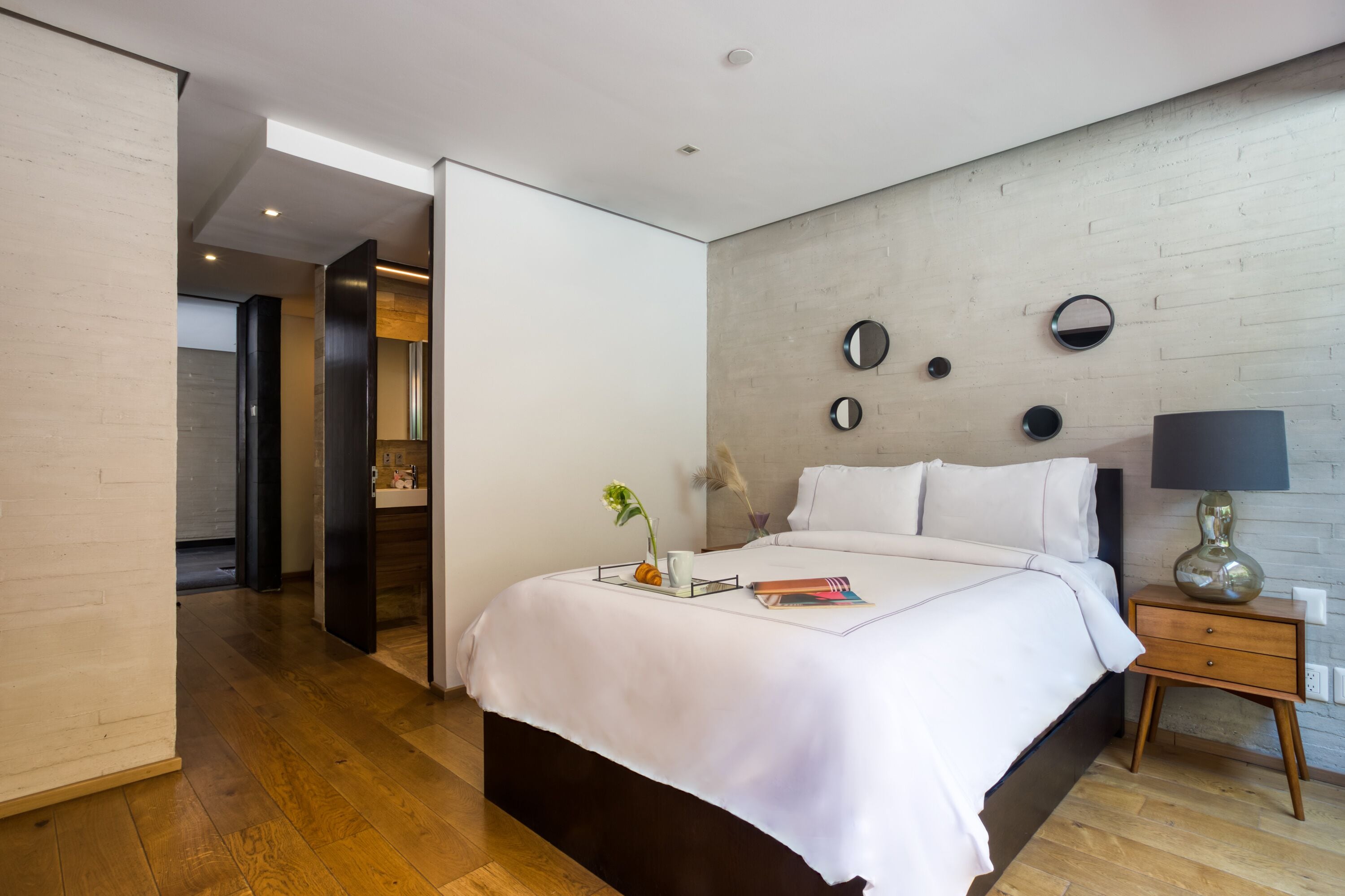 A modern bedroom with a bed, bedside table, and a wall-mounted mirror.