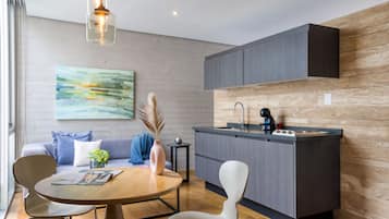 Una cocina moderna con armarios grises, encimera de madera y estufa integrada. Hay una zona de comedor con una mesa redonda y sillas, un jarrón con flores y un cuadro en la pared.