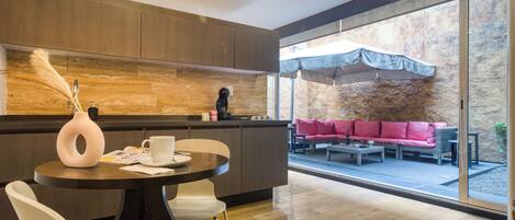 A modern kitchen with a dining area, a stone wall, and a seating area with a pink sofa and umbrellas.