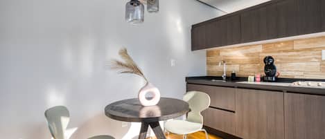 Une cuisine moderne avec des meubles de rangement en bois foncé, une table de salle à manger ronde accompagnée de deux chaises et des luminaires suspendus.