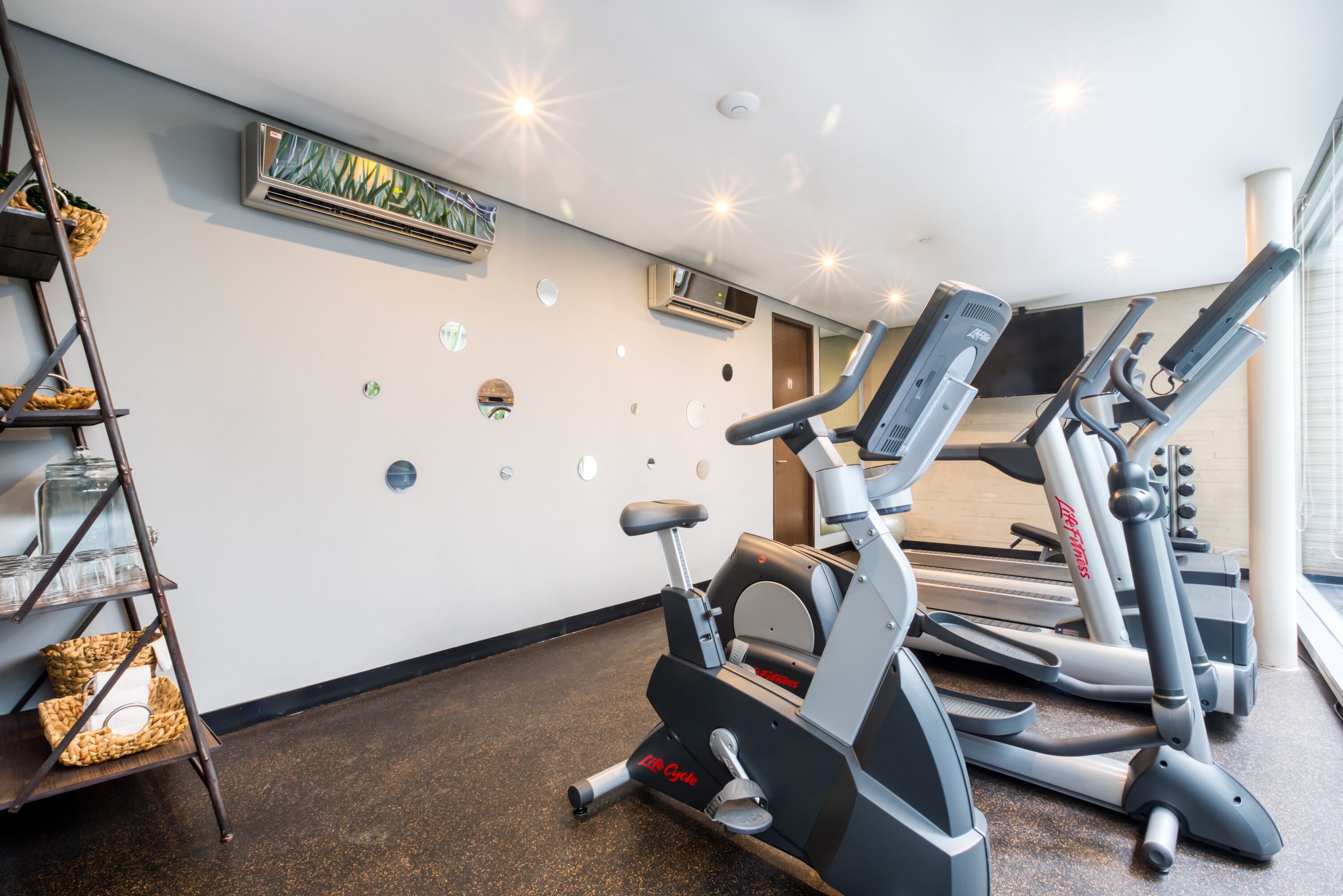 A gym with exercise equipment, a wall-mounted air conditioner, and a ladder with baskets.