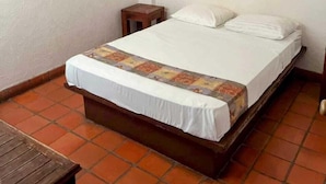 Una habitación pequeña y ordenada, con una cama individual, una mesita de noche de madera, una pequeña mesa y un ventilador de techo.