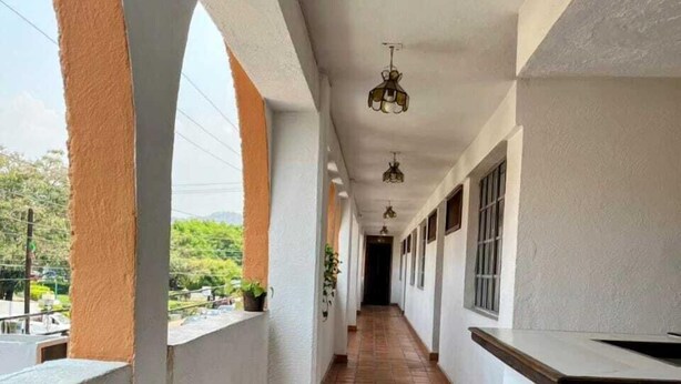 Un pasillo con paredes blancas, piso de baldosas y un balcón con barandilla.