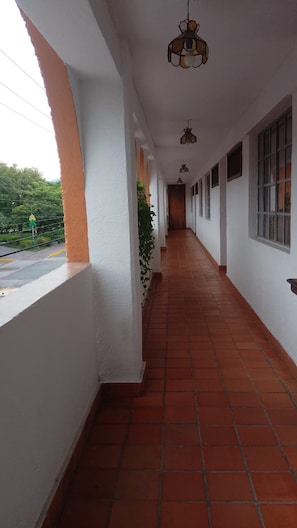 A corridor with white walls, red-tiled flooring, and hanging light fixtures.