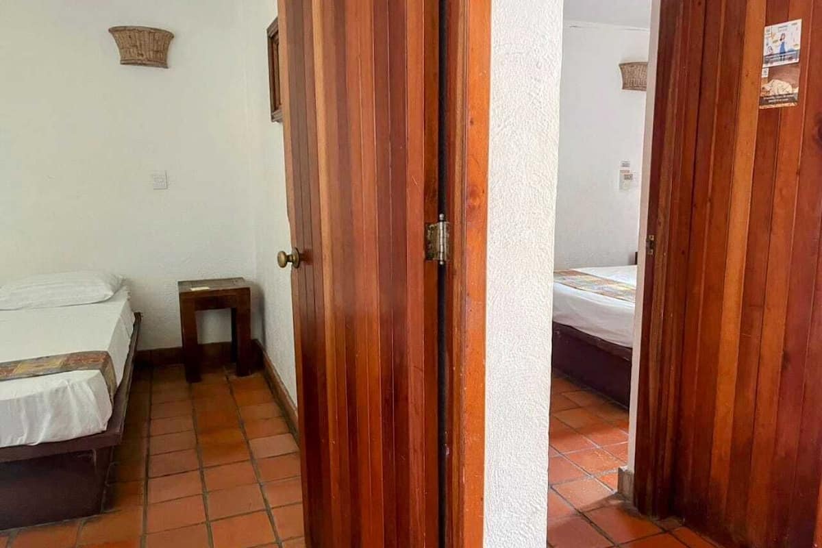 Une pièce avec deux lits, un petit tabouret en bois et une porte donnant sur une autre pièce.