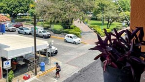 Vista desde un balcón sobre una calle con coches aparcados, un pequeño restaurante y un paso de peatones.