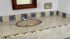 Un baño con lavamanos de azulejos, un espejo y un ventanal pequeño.