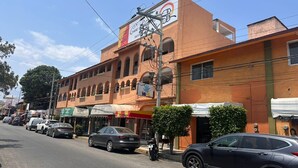 Un hotel con un cartel grande, muchas ventanas y coches aparcados a lo largo de la calle.