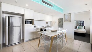 Una cocina moderna con armarios blancos, un refrigerador de acero inoxidable y un comedor con sillas blancas y una mesa de madera.