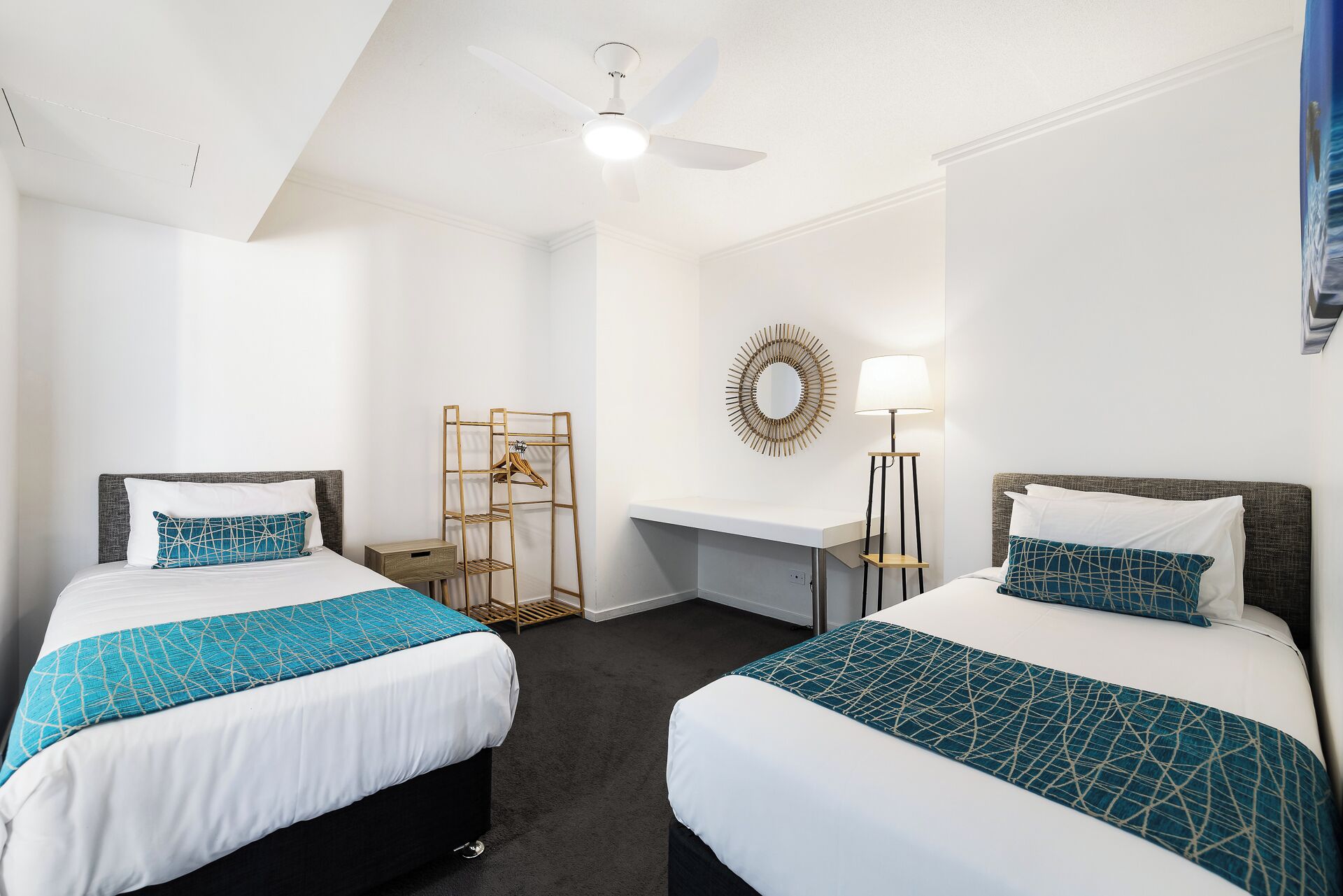 Hotellihuone, jossa on kaksi sänkyä, työpöytä, peili, lamppu ja kattotuuletin.