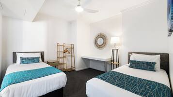Habitación de hotel con dos camas, un escritorio, un espejo, una lámpara y un ventilador de techo.